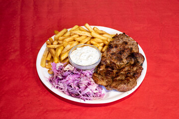 Pork chop served with chips or fries with coleslaw and dip, on a plate, with red tablecloth background

