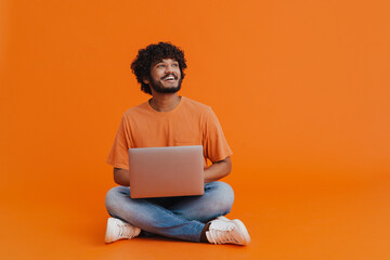 Young indian smiling man sitting with laptop in lotus pose