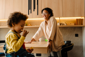 Young african mother wiping table looking at her little son