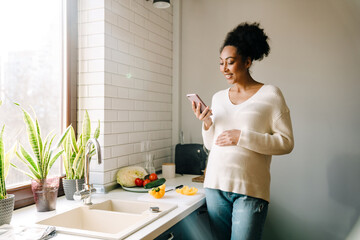 Adult beautiful smiling african pregnant woman looking on her phone