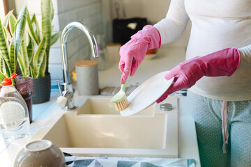 Female hands in pink gloves washing dishes with brush close-up