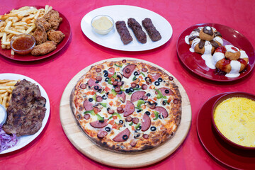 Pizza, sweet dumplings, fried chicken, pork chop and chips – selected restaurant dishes on a red background

