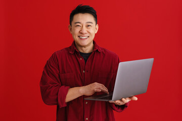 Asian young man wearing shirt laughing while using laptop