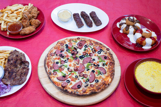 Pizza, sweet dumplings, fried chicken, pork chop and chips &ndash; selected restaurant dishes on a red background


