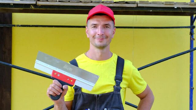 Portrait of a house repair and construction master with a close-up tool. A builder with a spatula in the exterior of the house. Plastering and finishing works, painter's services, repair of the facade