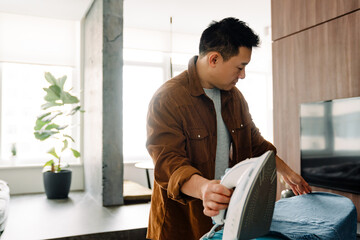 Asian young man ironing his shirt while doing housework