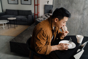 Asian man using tablet computer while having breakfast in kitchen