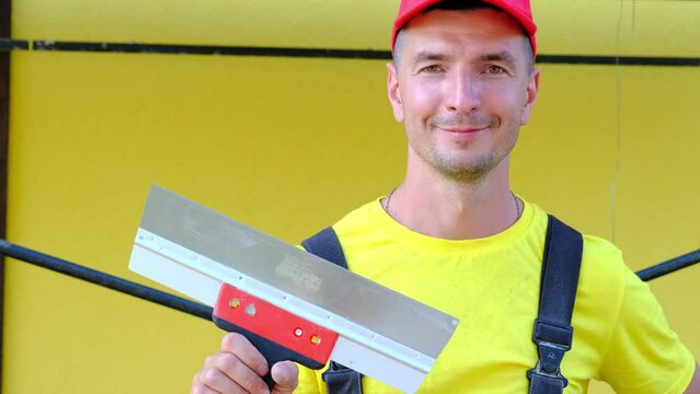 Portrait of a house repair and construction master with a close-up tool. A builder with a spatula in the exterior of the house. Plastering and finishing works, painter's services, repair of the facade