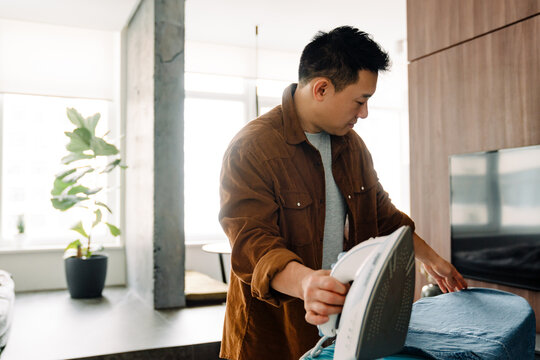 Asian Young Man Ironing His Shirt While Doing Housework