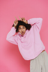 Young handsome stylish latin curly grimacing man in pink hoodie