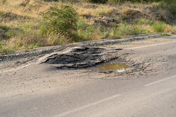 Deep hole in the road. Deformed asphalt surface with potholes melts from heat due to heavy overloaded trucks driving at hot summer days. 