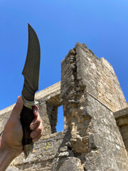 Closeup of male hand with handmade knife against blue sky and ruins, North Caucasus, Dagestan
