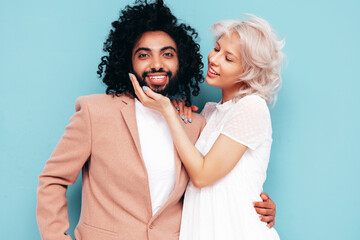 Smiling beautiful woman and her handsome boyfriend. Sexy cheerful multiracial family having tender moments on blue background in studio. Multiethnic models hugging. Embracing each other. Love concept