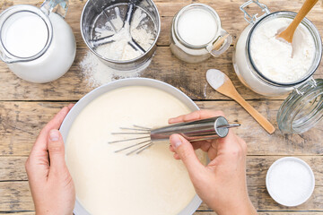 ingredients for making dough on a wooden table for pancakes, hands beat the dough with a mixer, top view