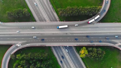 The drone flies over the track during traffic with many interchanges in different directions with a large number of cars that move one after another and change lanes to the desired exit from the track - obrazy, fototapety, plakaty