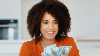 Portrait indoors wealthy happy smiling exited successful African American woman counting dollar...
