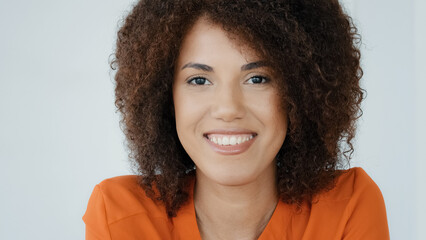 Close-up female face with ideal dark smooth skin. Healthy skincare cosmetic procedures. Satisfied lady client of hairdressing salon with curly hair. Portrait African American girl smiling posing happy