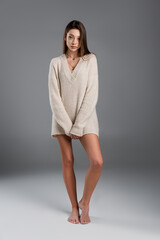 full length of barefoot woman with slim naked legs wearing long sweater on grey background