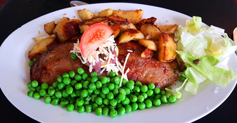 Danish traditional dinner plate with schnitzel, chips and green peas - and a lemon slice with capers, anchovy and horseradish on top
