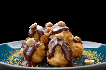 Profiteroles dessert with hazelnuts on a black background. With selective focus