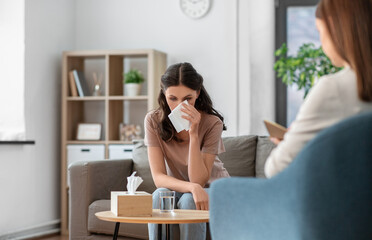 Fototapeta premium psychology, mental health and people concept - crying woman patient wiping tears with paper tissue and psychologist at psychotherapy session