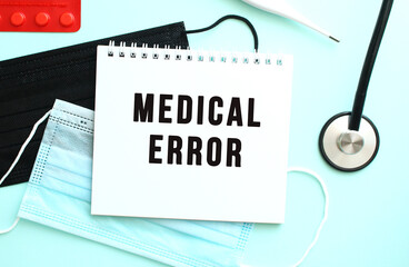 The text MEDICAL ERROR is written in a notebook that lies on a blue background next to a medical masks