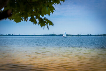 A beautiful lagoon with clear water. A lonely sailboat in the background. Sunny day. Holidays. Lake Dziećkowice, Poland