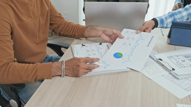 Cropped slowmo of unrecognizable male colleagues analyzing financial statistics while having business meeting in office