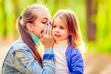 Mom whispers daughter in her ear. Walk in the summer forest