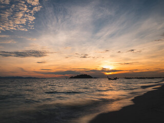 Scenic view of sunrise and motion blurred wave on tropical island beach with local longtail boat silhouette and small island. Sunrise beach, Koh Lipe Island. Satun, Thailand. long exposure.
