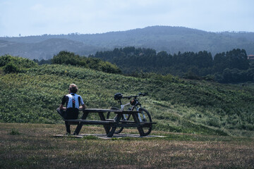 Cyclist sitting with the bike leaning on a wooden table looking towards the mountains