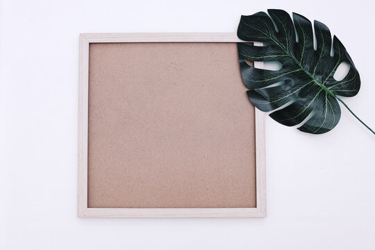 Wooden photo frame mockup with artificial plant on white background. Flat lay, top view, copy space, square.