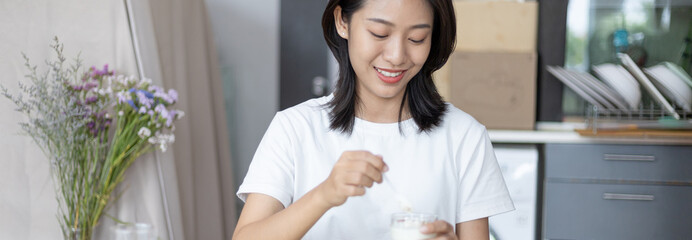Half-Japanese woman eats yoghurt with cereal for breakfast in room, Healthy food and digestive...