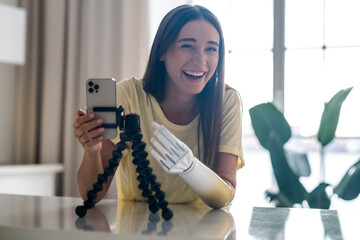 Girl blogger with bionic arm using phone, live streaming social media at home, woman with disability prosthetic limb, working online remotely from home using artificial prosthetic limb