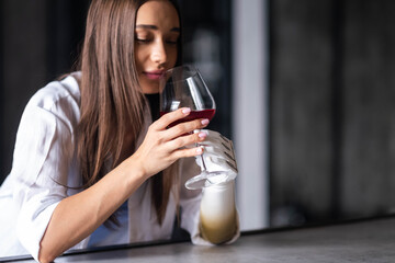 Calm thoughtful girl holds glass of wine in bionic arm at home, woman with artificial prosthetic limb