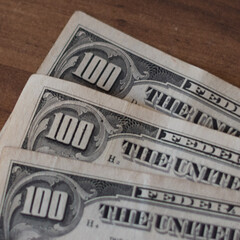 Billetes de 100 dolares apilados en secuencia sobre una mesa de madera, billetes gastados