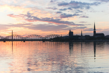 Beautiful sunset skies and their reflection in the calm waters of a wide river. Two bridge contours are visible.	