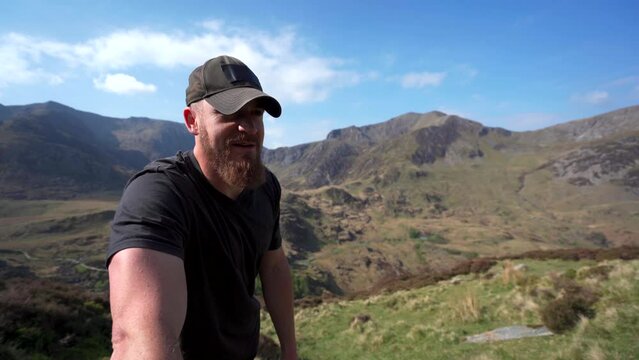 A man wearing a baseball cap talking to the camera in the mountains