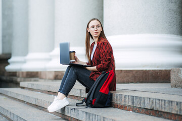 Outdoor portrait of female student with coffee cup and laptop. Girl student has coffee break after lectures