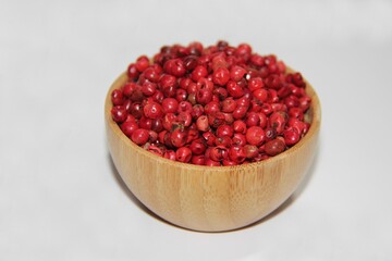 Pink pepper (Schinus terbinthifolia). In a wooden bowl isolated on a blurred background. Selective focus. Also known as: Aroeira-Red, Aroeira-pimenteira or Poivre-rosa.