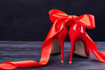 Close up back view red high heels and ribbon. Grey wooden desk.