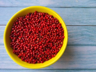 Pink pepper (Schinus terbinthifolia). In a yellow bowl isolated on a gray background. Selective focus. Also known as: Aroeira-Red, Aroeira-pimenteira or Poivre-rosa.