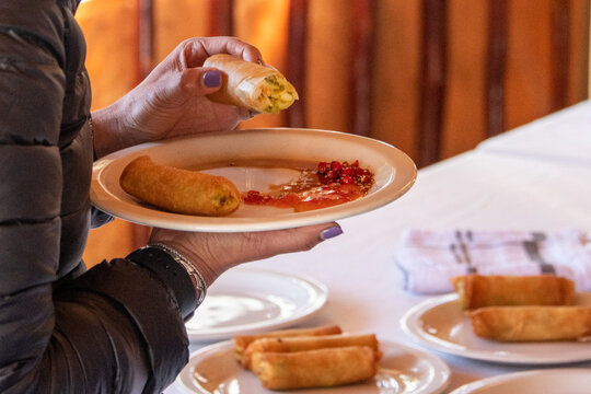 Freshly Prepared Egg Rolls Being Eaten With Sweet Chili Sauce By Someone Wearing A Puffer Jacket With Purple Nailpolish