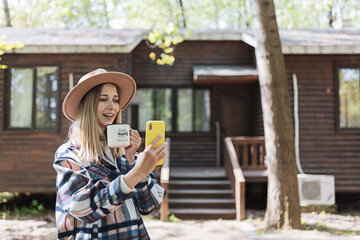 Young stylish caucasian woman 30-35 years old wearing casual clothing shirt and cowboy hat. Influencer using social media via mobile phone. Person enjoys life at morning during summer adventure in