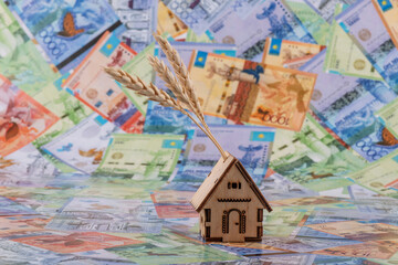 Symbolic wooden house and ears of wheat against the background of Kazakh banknotes - tenge