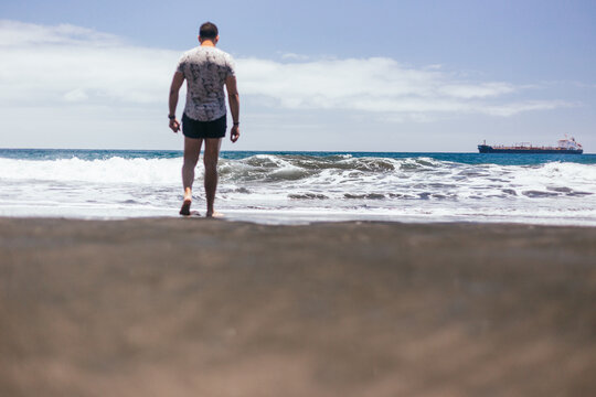 Beautiful young man enjoying and walking along black sand beach