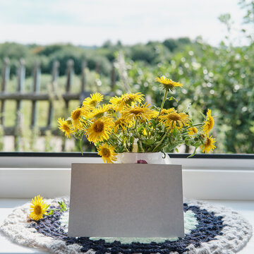 Greeting mockup scene on window sill of rural house. Blank paper, bouquet of wildflowers