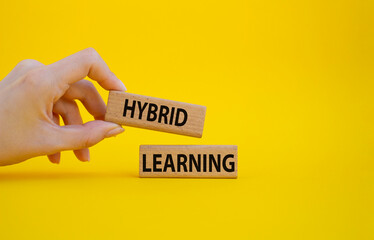 Hybrid learning symbol. Concept word Hybrid learning on wooden blocks. Beautiful yellow background. Businessman hand. Business and Hybrid learning concept. Copy space