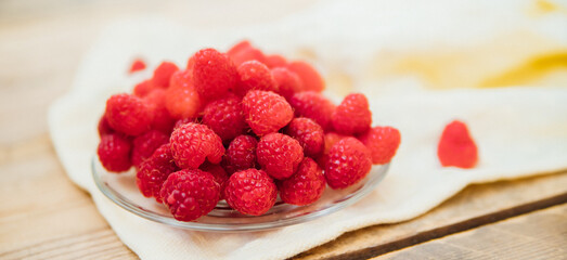Raspberry fruits on a small saucer, a bunch of summer berries on a wooden background. Summer background. Juicy appetizer or dessert.