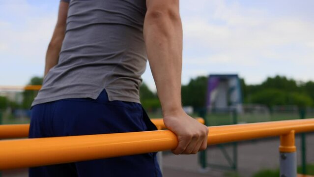 Caucasian gymnast performs push-ups on the uneven bars on the sports field of the stadium. A young athlete in a sports uniform performs gymnastic exercises on parallel bars